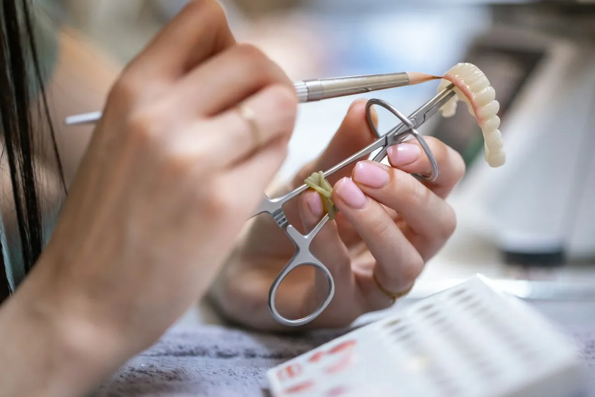 Manos femeninas con pinza y espátula trabajando una prótesis dental parcial sobre mesa de trabajo — laboratorio de prótesis dental Consciencia Odontológica